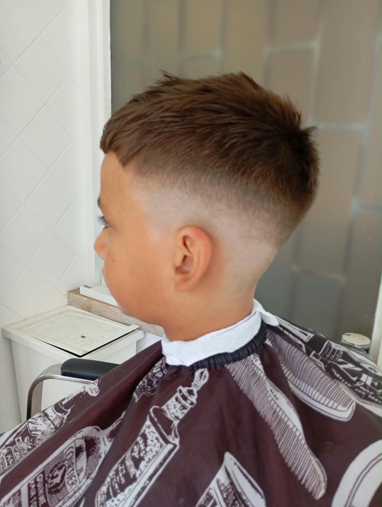A mesma criança depois do corte, com skin fade e topo em pico